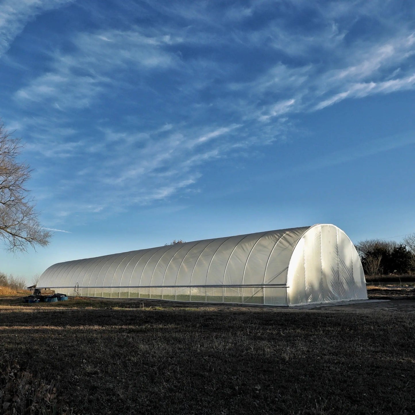 Large all-metal hoop house greenhouse in a rural farm setting under blue sky