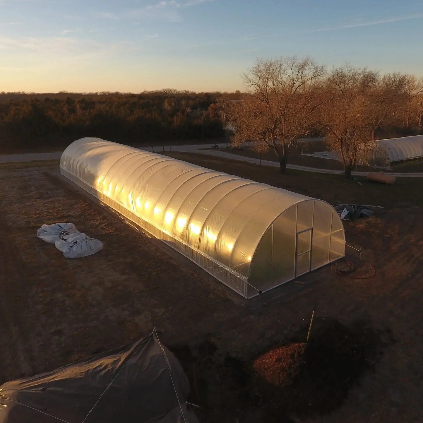All-metal hoop house greenhouse on a farm at sunset, surrounded by bare trees and fields
