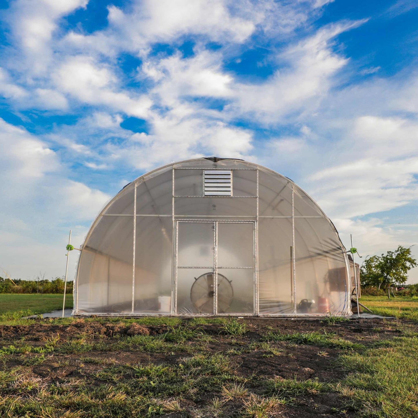 All-metal hoop house greenhouse with rounded roof on grassy field under blue sky
