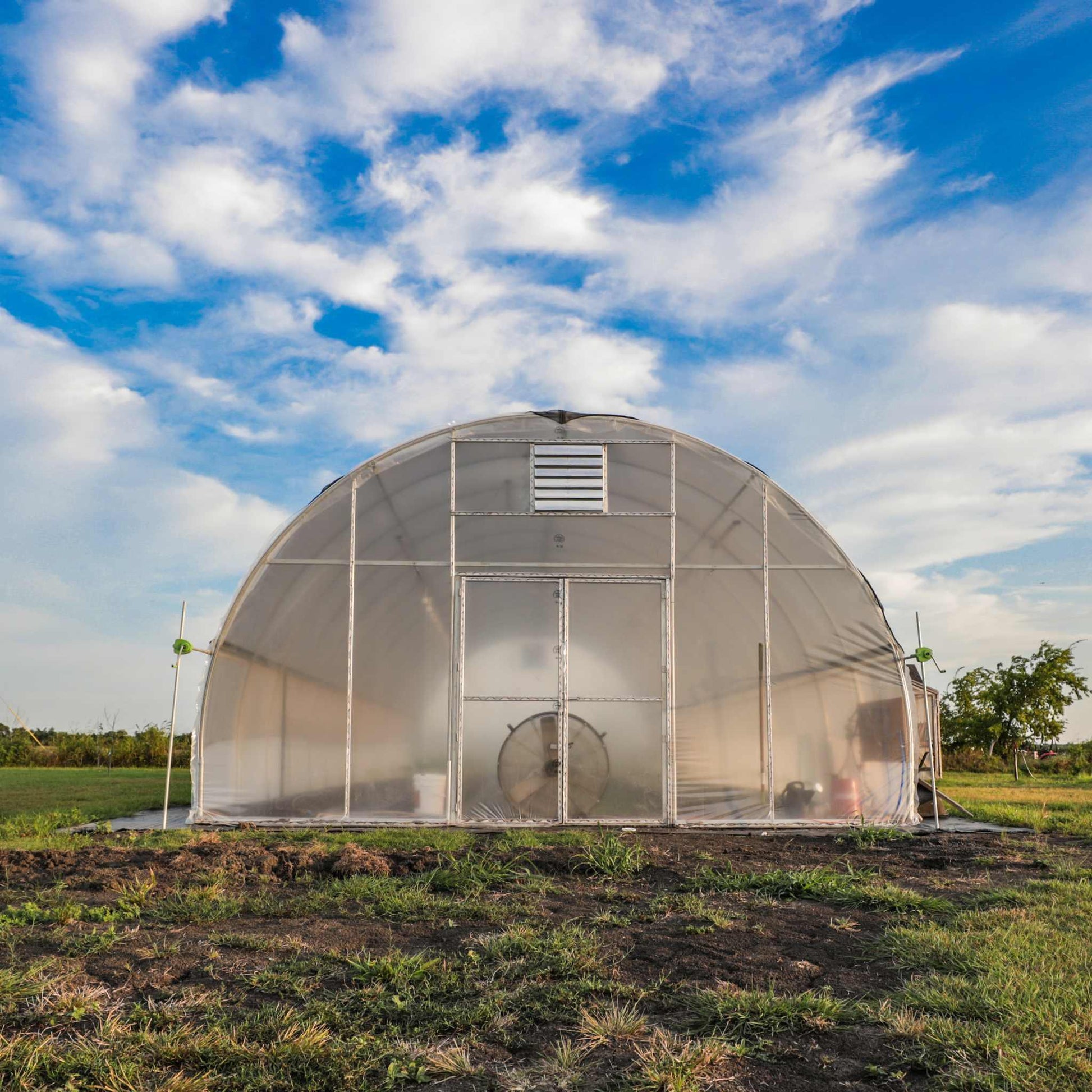 All-metal hoop house greenhouse with rounded roof on grassy field under blue sky