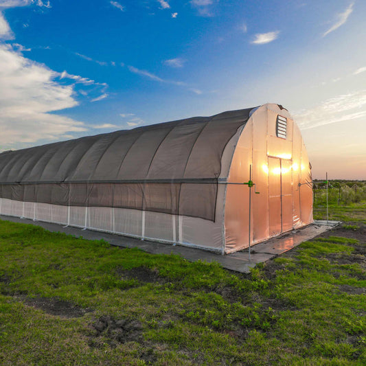 Metal hoop house greenhouse with roll up sides in a grassy field at sunset