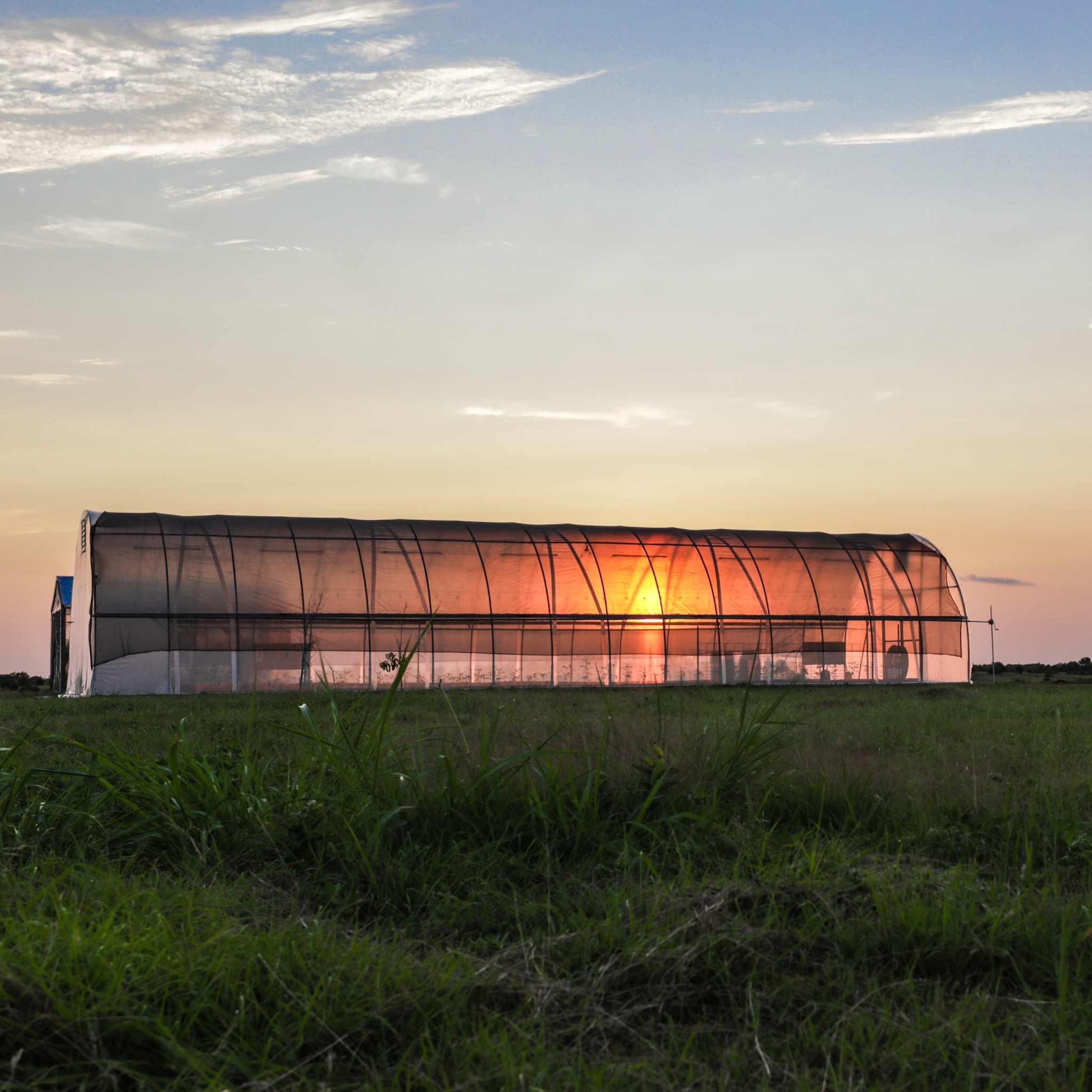 20 foot round metal greenhouse with shade cloth at sunset in open field